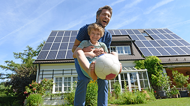 Vater mit seinem Sohn vor einem Haus mit einer Photovoltaik-Anlage, Verbraucherzentrale Energieberatung