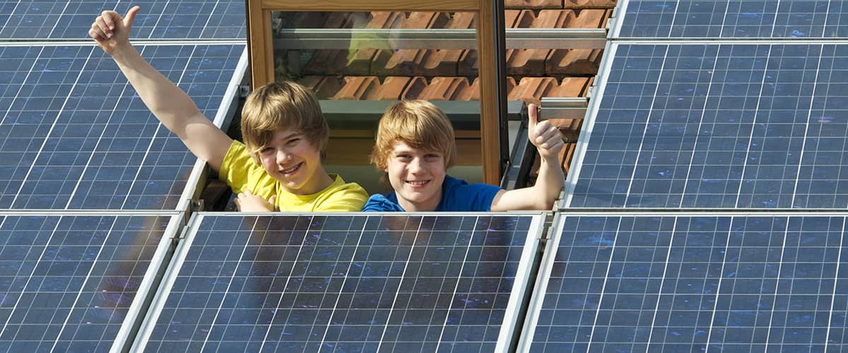 Erneuerbare Energie: Kinder winken aus Dachfenster umgeben von Photovoltaikanlage
