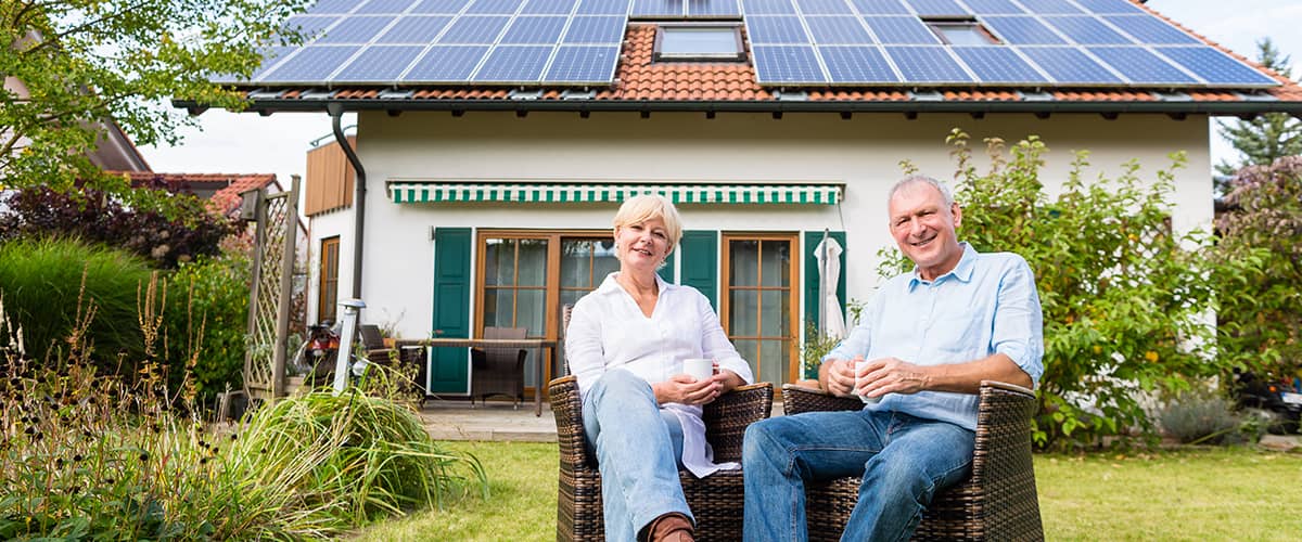 Erneuerbare Energie - Photovoltaik: Paar sitzt im Garten vor Haus mit Photovoltaikanlage