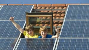 Erneuerbare Energie: Kinder winken aus Dachfenster umgeben von Photovoltaikanlage
